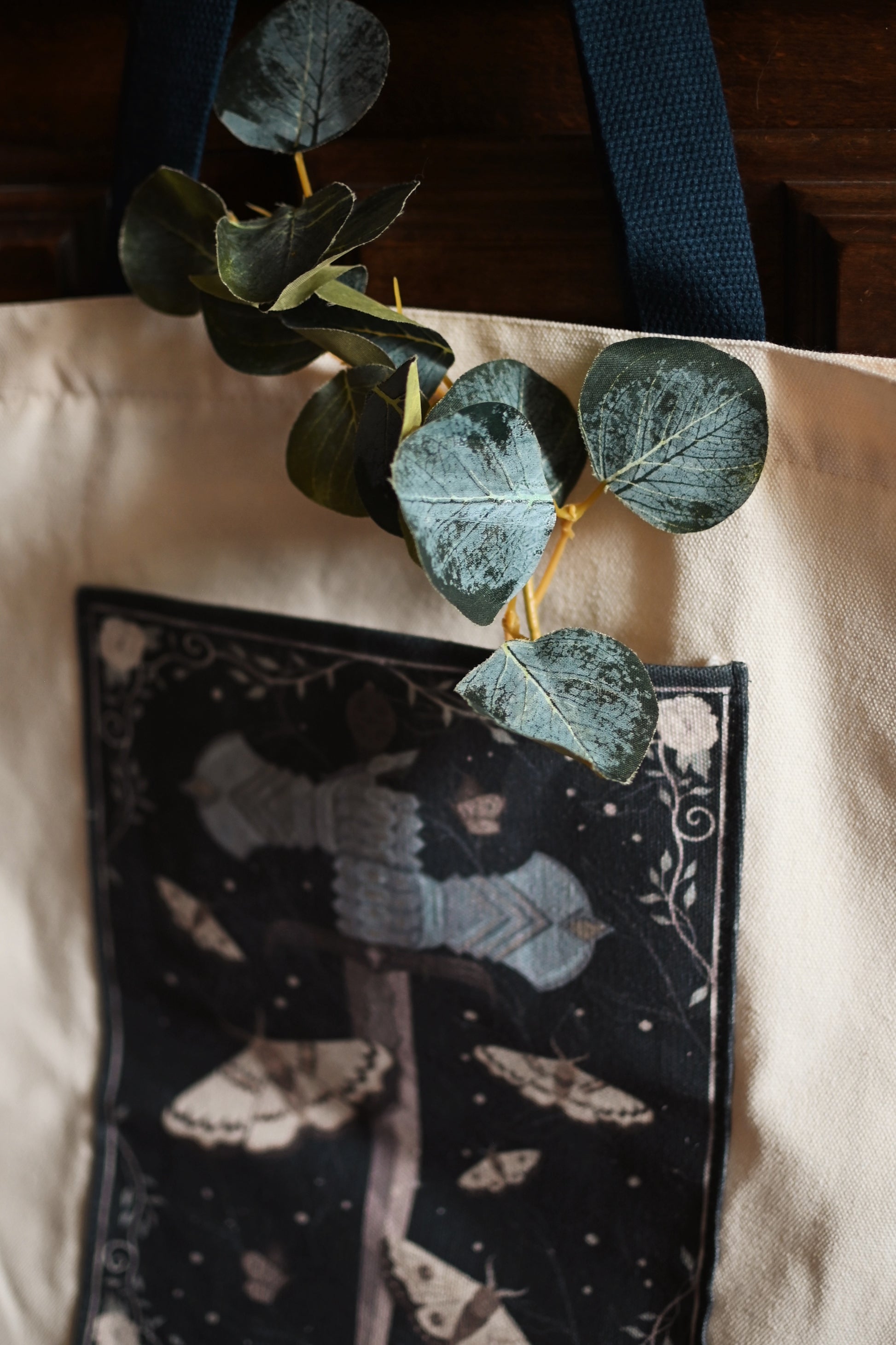 Green leaves on a black pouch with moth design on a beige surface