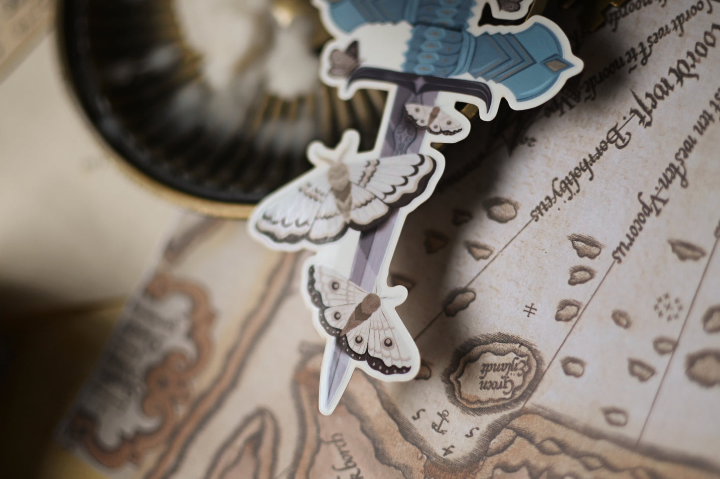 Close up of The Knight and the Moth sticker showcasing the sword holding the sword surounded by moths.