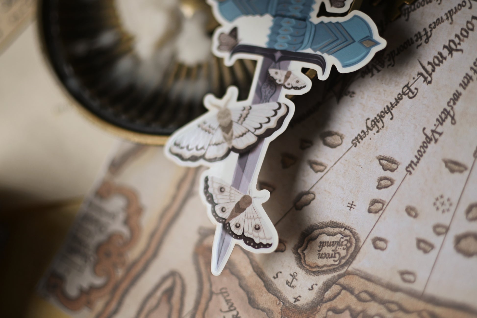 Close up of The Knight and the Moth sticker showcasing the sword holding the sword surounded by moths.