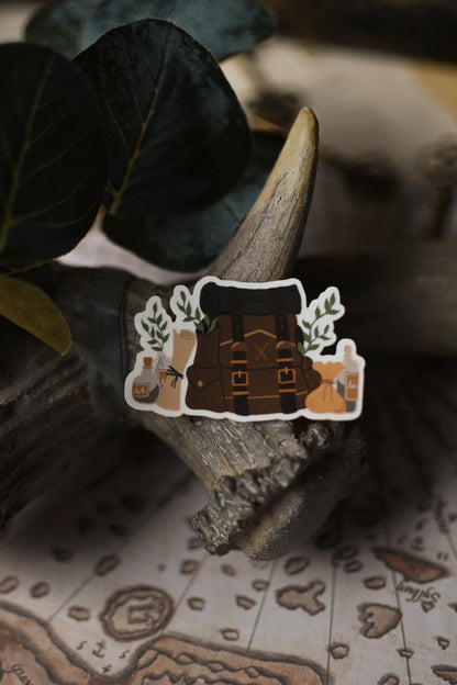 Sticker of an adventurer's backpack on a wooden surface with a map in the background.