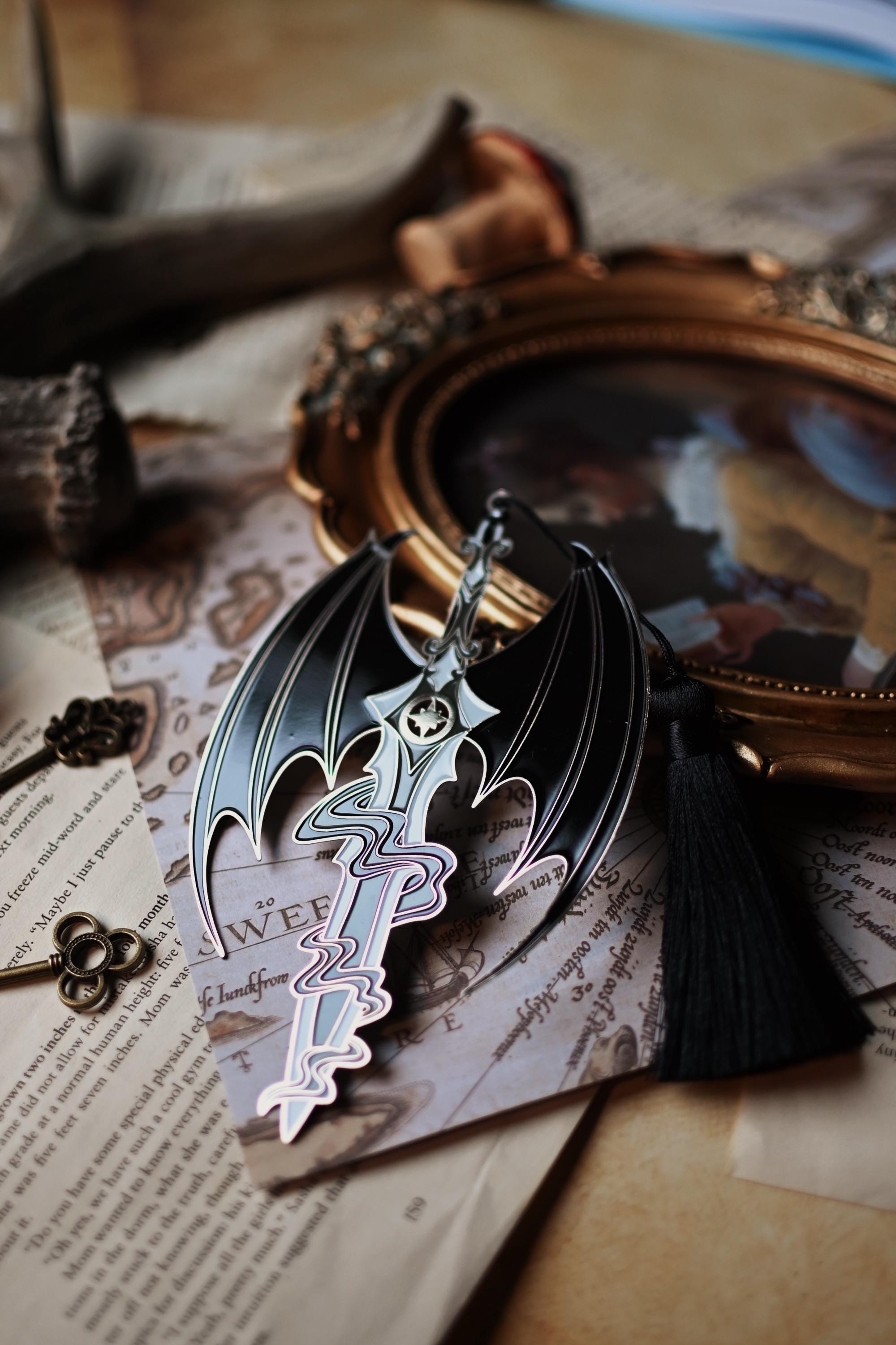 The officially licensed a court of thorns and roses bookmark inspired by the character of Azriel Shadowsinger. The enamel bookmark features a sword worthy of the night court and is surounded by the illyrian wings. 