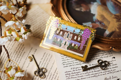 An enamel pin featuring an illustration of Bridgerton House with purple flowers and a yellow frame, placed on a surface with a vintage aesthetic with the shine of sunlight.