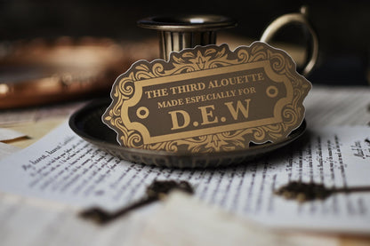 A sticker with vintage design, gold and black in color, with the text 'THE THIRD ALOUETTE especially for D.E.W inspired by Rebecca Ross' Devine Rivals.