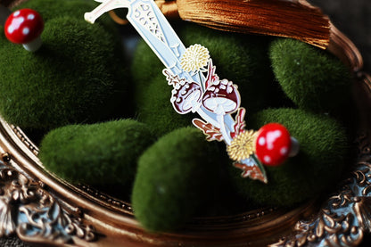 Close up shop of the fae queen sword bookmark that focuses on the tip of the sword which has been interwoven with mushrooms and florals. 