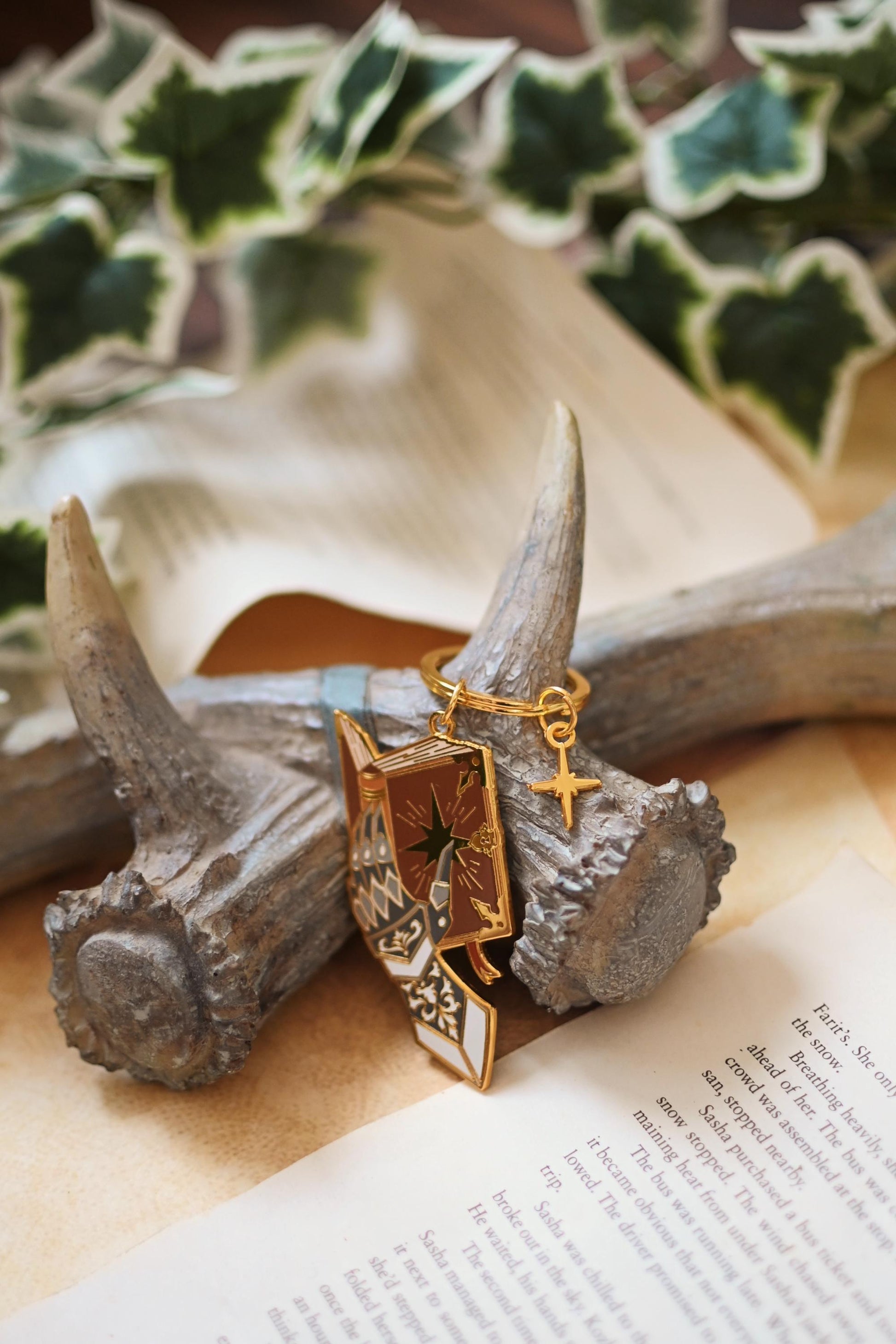 A wide shot of the Fairytale Gauntlet gold metal keychain designed as a gauntlet with a star detail, placed on a wooden surface with a foil backing card.
