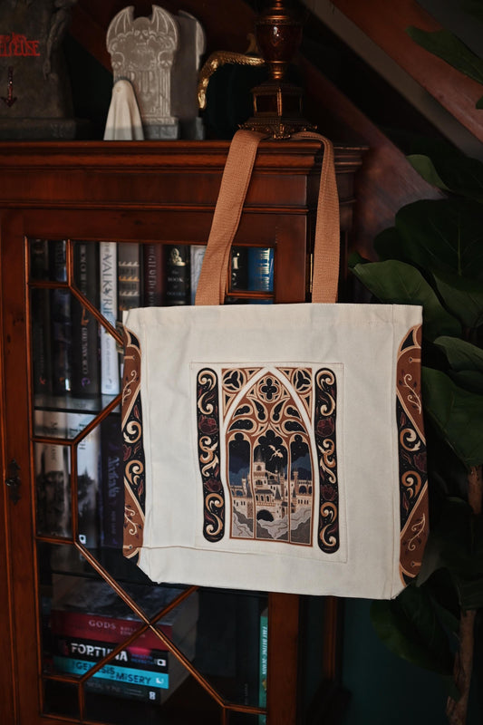 No One Designs Fantasy Castle tote book bag design hanging up to showcase the front design of the window pain looking out onto a castle. 