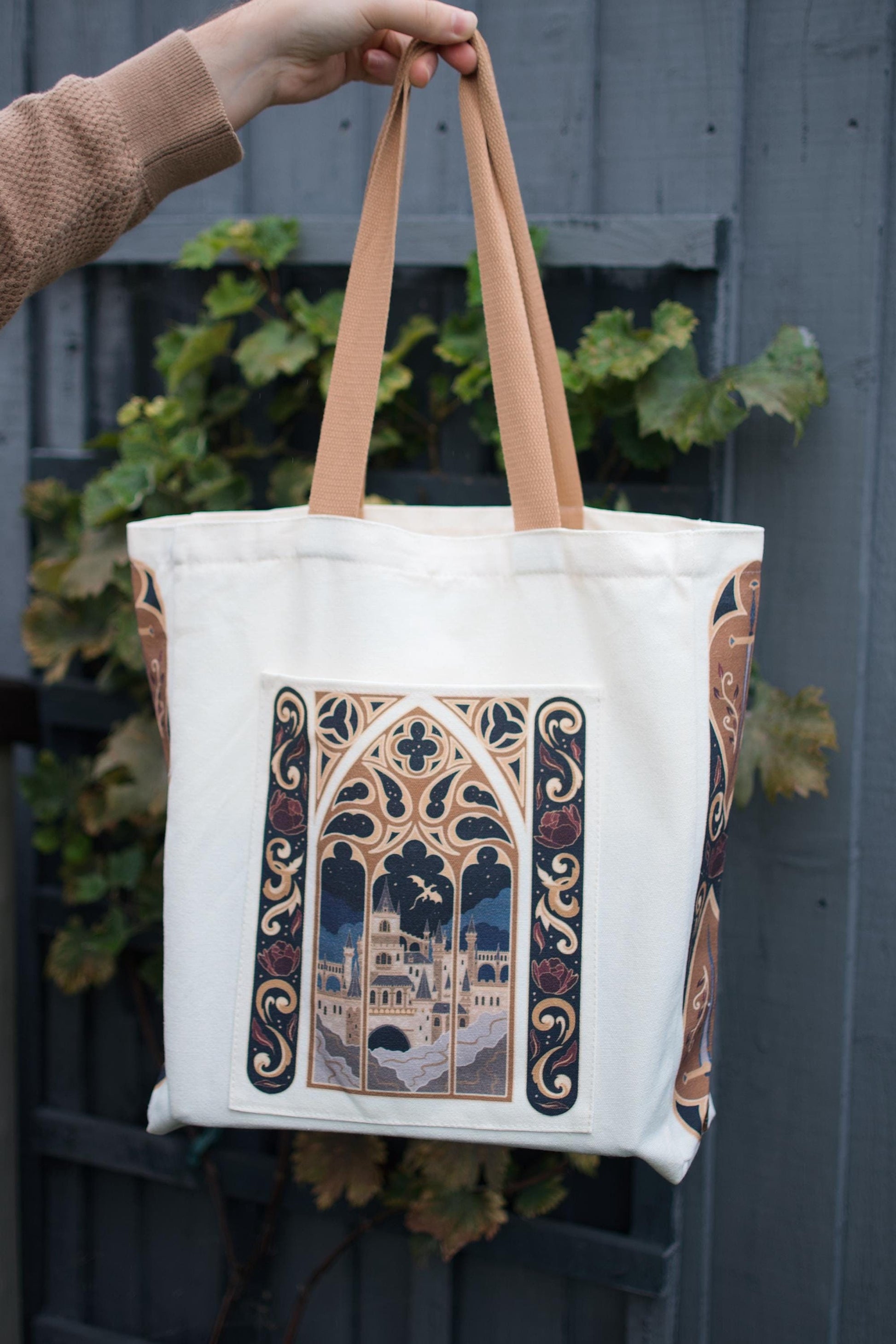 Chloe holding up the fantasy book bag tote against a blue background with the tote bag filled with items to showcase the bag in action. 
