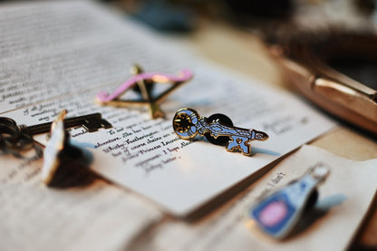 A close up show of the blue enamel key pin resting against open pages of a book surrounded by the other pins of the collection.