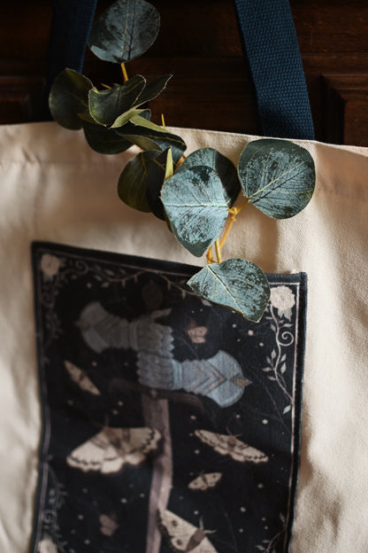 Green leaves on a black pouch with moth design on a beige surface