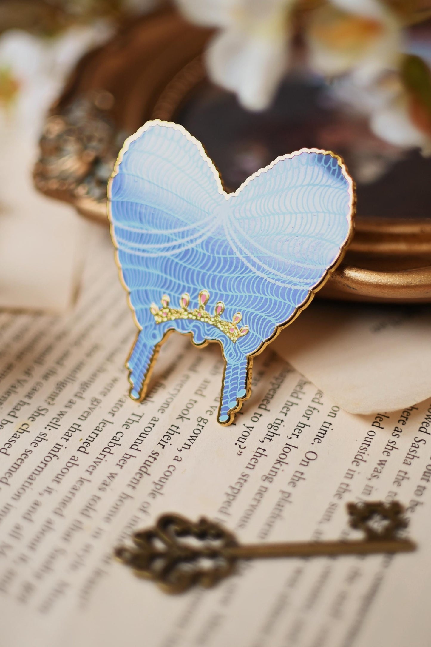No0neDesigns Bridgerton Collection featuring the Queen Charlotte Wig enamel pin. The pin is help upright against a tip of a mirror to show the silk pint detailing of the wig and crown detailing too aginst the light.