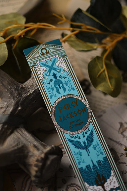 Close up of the Percy Jackson Book Spine inspired decorative bookmark with blue and gold design resting on a map with antlers and keys in the background
