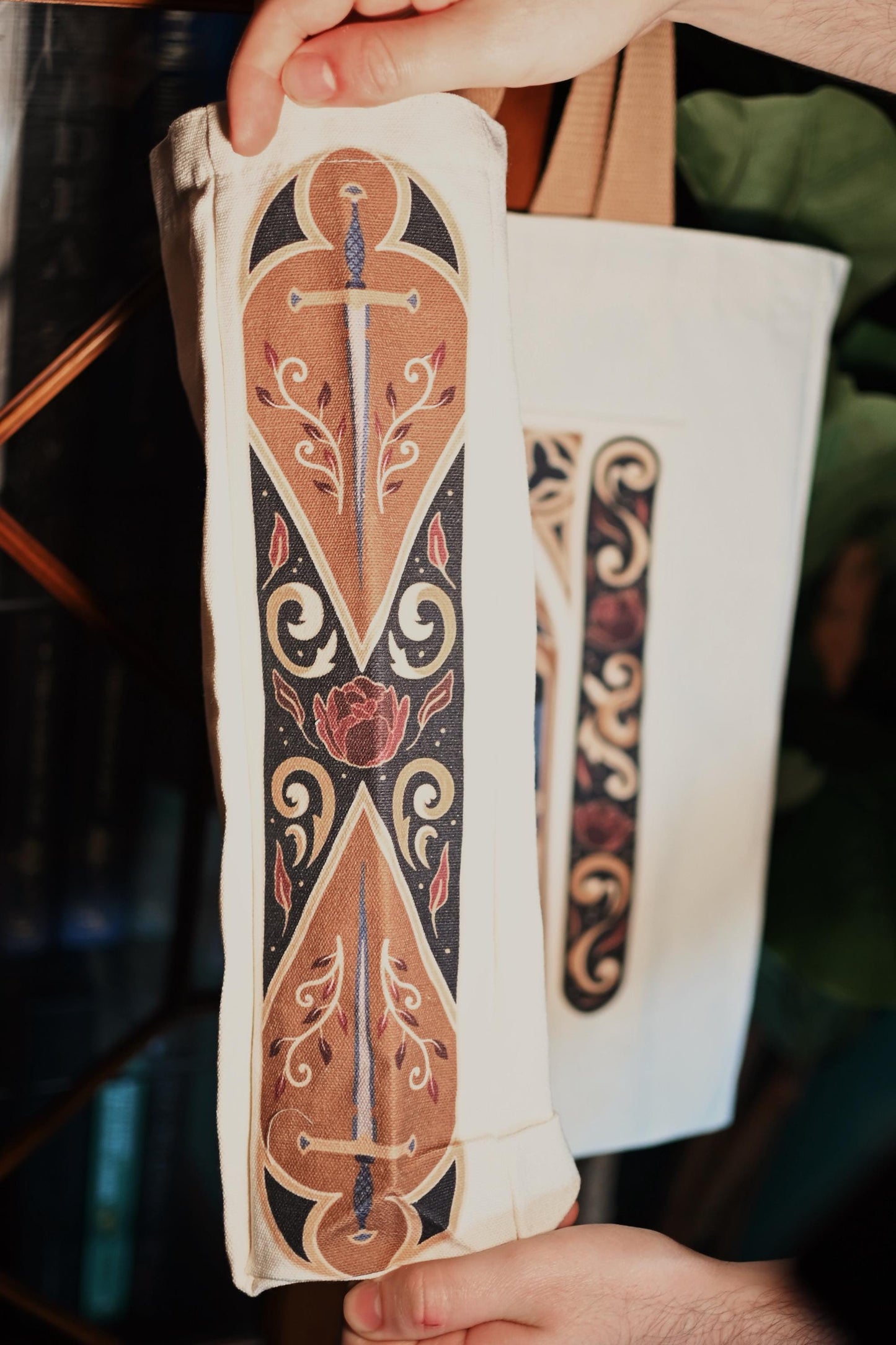 Close up image of the side panel of the fantasy window tote bag showcasing the design with swords and red leaves. 