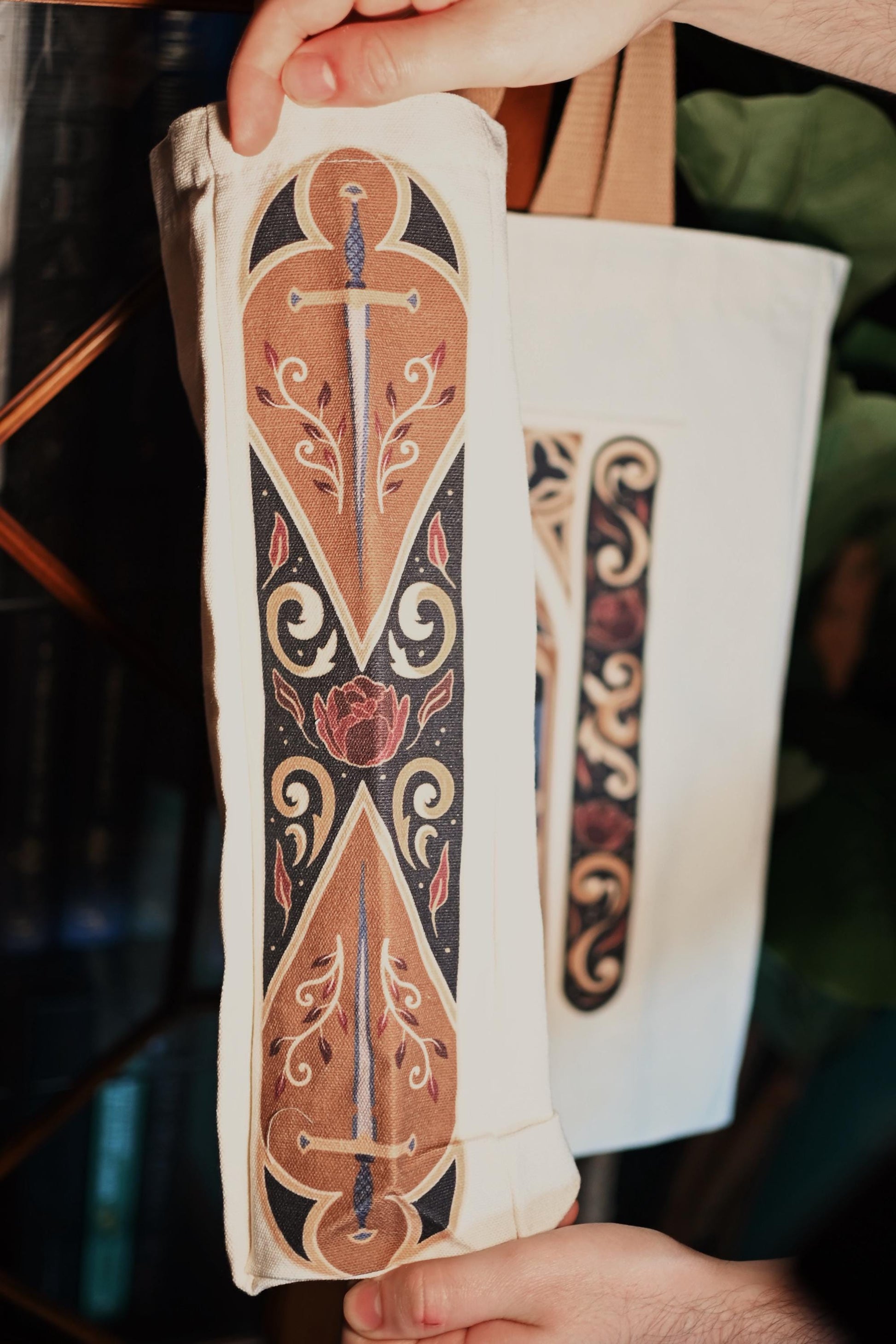 Close up image of the side panel of the fantasy window tote bag showcasing the design with swords and red leaves. 