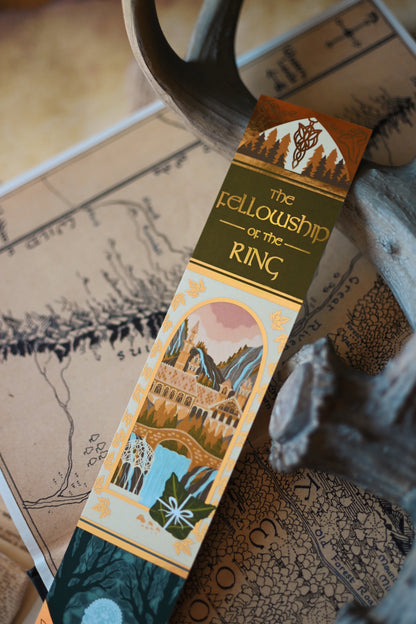 No0neDesigns The Fellowship of the Ring foil bookmark with the sunlight relfecting on the foil. The bookmark is propped up slightly and in the background is a blurred map of middlearth. 