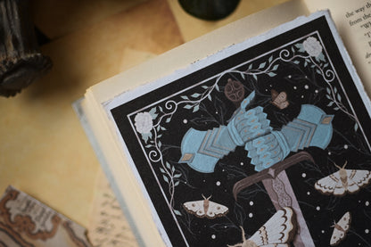 The Knight and the Moth inspired art print featuring a black and white illustration of a figure in blue gauntlets, surrounded by moths, on a wooden surface.