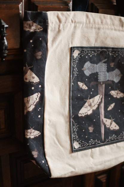 The Knight and the Moth inspired tote bag with decorative design hanging on a wooden cabinet - the image showcases a close up of the side panelling.