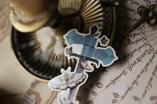 Close up of The Knight and the Moth sticker showcasing the blue gauntlets holding the sword surounded by moths. 