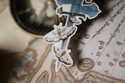 Close up of The Knight and the Moth sticker showcasing the sword holding the sword surounded by moths. 
